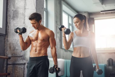 Modern bir spor salonunda halterleri uyumlu bir şekilde kaldıran fit bir çift hem formda hem de ortaklıklarını sergiliyor.