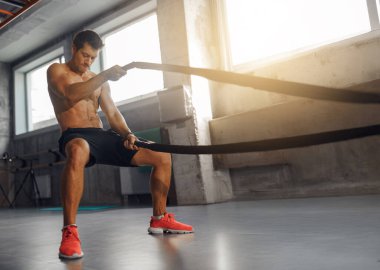 Hareketli bir spor salonunda, bir sporcu güçlü ve dayanıklı olmak için savaş halatlarıyla sıkı antrenman yapar.