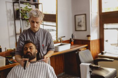 Yetenekli bir berber, şık ve çağdaş bir berber dükkanında müşterisini titizlikle tımar ediyor.