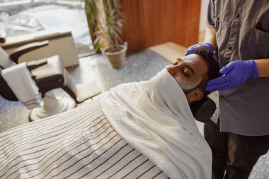 Şık ve şık bir berber dükkanında sakal tıraşı ve yüz bakımı yapan bir adam.