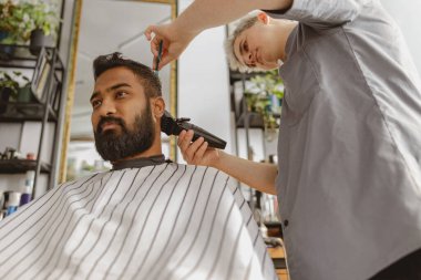 Modern bir kuaförde, yetenekli bir berber müşterinin saçını ustalıkla keser, çağdaş tımar tekniklerini sergiler.