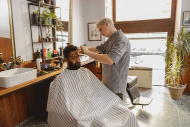 Yetenekli bir berber, modern bir salonda bol doğal ışık içeren şık ve modaya uygun bir saç kesimi sağlar.