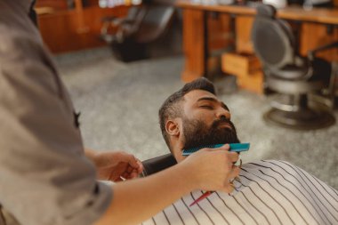 Şık bir berber dükkanında, çok yetenekli bir berber, müşterisinin sakalını titizlikle tıraş eder.