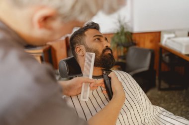 Bir adam, modern ve şık bir berber dükkanında sakalını ustalıkla kestirip gerçek tımar sanatını sergiliyor.