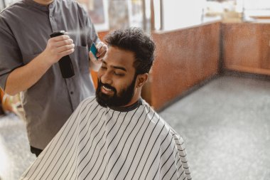 Parlak ve modern bir kuaför ortamında, yetenekli bir berber, müşterinin saçını dikkatlice şekillendirir.