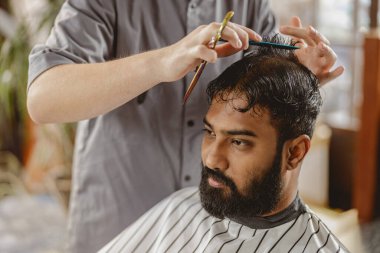 Bir berber modern ve çağdaş bir kuaför salonunda ustalıkla saç kesiyor, buduyor ve şekillendiriyor.