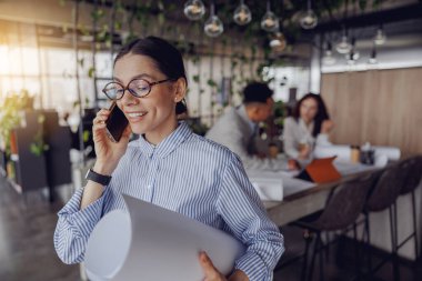 Neşeli ve gülümseyen bir profesyonel çağdaş ofis ortamında bir telefon görüşmesi yapıyor.