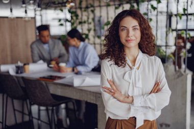Kendine güveni olan bir kadın modern bir ofiste duruyor ve ortak çalışma alanında liderlik yeteneklerini sergiliyor.