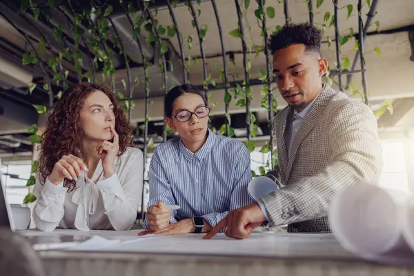 Çeşitli profesyonellerden oluşan bir grup, yeşil, çağdaş ofis ortamında gelecek planlarını tartışıyor.