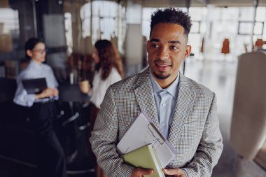 Gülümseyen bir işadamı, modern bir ofiste iş arkadaşlarıyla uğraşırken, güvenilir bir şekilde önemli belgelere sahiptir.