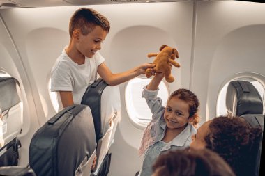 İki neşeli çocuk uçarken sevimli bir oyuncak ayıyla oynayarak harika vakit geçiriyorlar, inanılmaz seyahat anları yakalıyorlar.