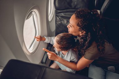Bir anne ve çocuğunun bir uçak penceresinden dışarı bakıp birlikte keşfe çıktığı neşeli bir an.
