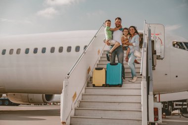 Çocuklarıyla birlikte neşeli bir aile heyecanlı bir yolculuğa hevesle hazır bir şekilde havaalanından uçağa biniyor.