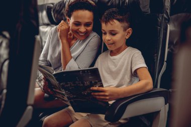 Bir anne ve küçük oğlu, renkli bir dergiye bakarken uçakta keyifli ve keyifli bir anı paylaşıyorlar.