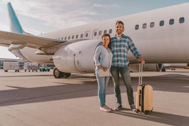 Neşeli bir çift, bir uçağın yanında mutlu bir şekilde poz verir. Yolculuğun ve heyecanlı maceranın gerçek ruhunu tamamen somutlaştırır.