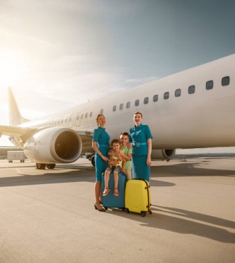 Mutlu ve neşeli bir aile, yoğun havaalanındaki bir uçağın yanında dost hosteslerle iletişim kurarken görülüyor.