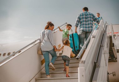Neşeli bir aile, yaklaşan tatilleri için heyecanlı bir şekilde uçağa binmek için merdivenlerden birlikte çıkıyor.