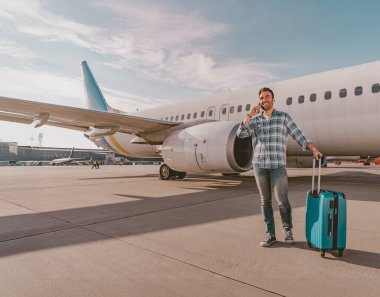 Renkli bir bavulu olan mutlu bir yolcu, unutulmaz bir maceraya hazır büyük bir uçağın yanında gururla durur.