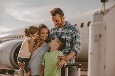 Neşeli bir aile, yolculuklarından önce heyecanlı bir şekilde maceralarını kucaklayarak, yoğun havaalanında güzel vakit geçirir.