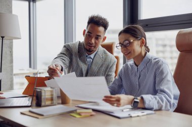 İki profesyonel, işbirliği ve verimliliği artırmak amacıyla modern bir ofiste önemli belgeleri tartışıyor