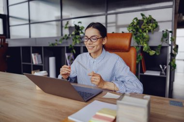 Odaklanmış bir kadın şık ofisinde uzaktan kumandayla çalışır, rahat bir şekilde oturur ve bilgisayarını kullanır..
