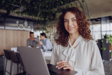 Kendine güvenen ve kararlı bir kadın şık ve enerjik bir ofis ortamında dizüstü bilgisayarı üzerinde çalışıyor.