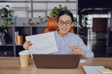 Yetenekli profesyonel bir kadın modern çalışma alanında çeşitli veri analiz çizelgeleri sergiliyor.