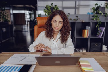 Canlı yeşilliklerle dolu modern ve şık bir ofiste özenle laptopuyla çalışan odaklanmış bir kadın.