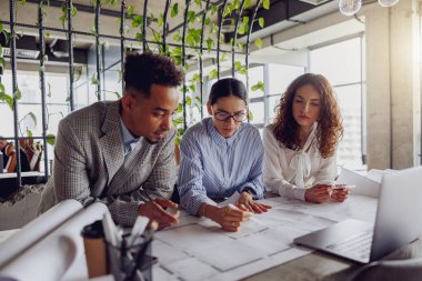 Çeşitli ve yetenekli bir ekip modern bir çalışma alanı içinde yenilikçi mimari planlar üzerinde işbirliği içinde çalışıyor.