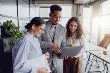 Modern bir ofis alanında, takım üyeleri bir dizüstü bilgisayar kullanırken ilgi çekici bir tartışma yoluyla işbirliği yapıyorlar.