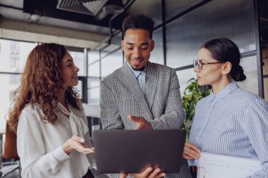 Çok yetenekli profesyonellerden oluşan çeşitli bir grup, çağdaş bir ofis ortamında dizüstü bilgisayar üzerinde işbirliği yapıyor.