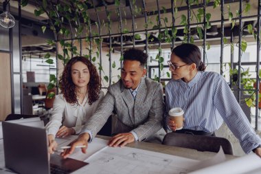 Yetenekli profesyonellerden oluşan çeşitli bir ekip, şık, yeşil bir ofis alanında önemli bir proje üzerinde işbirliği yapıyor.