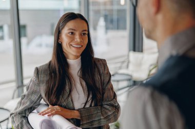 Kendine güvenen bir kadın, modern ofis ortamında ilham verici bir sohbete girişerek sıcak bir şekilde gülümser.