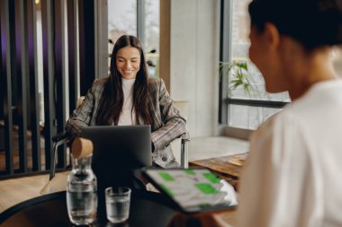 Moda bir kafede, iki kadın çalışmak için dizüstü bilgisayar ve tablet kullanırken fikirler hakkında canlı bir tartışmaya giriyorlar.