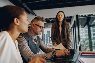 Üç profesyonel, çağdaş bir ofis ortamında dizüstü bilgisayarla ortak bir tartışmaya giriştiler..