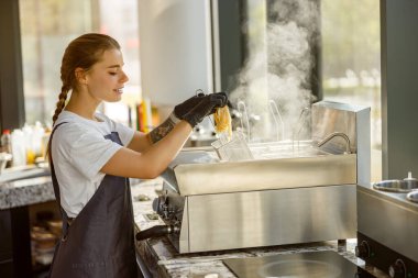 Odaklanmış bir barista kahve yapar. Parlak, modern bir kafede buhar yaratır.