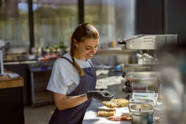 Eldiven giyen neşeli bir aşçı modern bir mutfak ortamında bulaşıkların karmaşık hazırlıklarına konsantre olur.