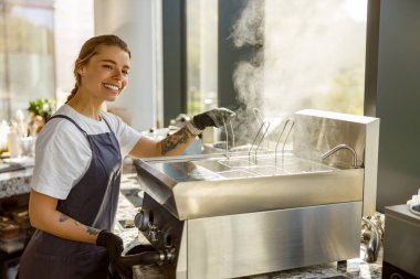 Gülümseyen bir barista kahveyi ustalıkla hazırlar, hareketli bir kafe atmosferi sergiler.