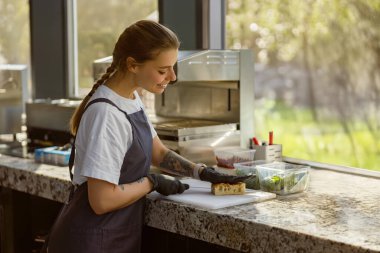 Kendini işine adamış ve odaklanmış genç bir şef özenle taze malzemeler hazırlıyor. Parlak, modern bir mutfak ortamında.