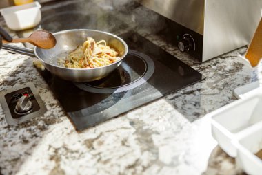 Bir tencere buharlı makarna, çağdaş bir mutfaktaki zarif ve modern bir indüksiyon sobasında ustaca pişiriliyor.