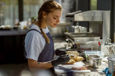 Parlak ve şık bir mutfakta, yetenekli ve odaklanmış bir şef titizlikle lezzetli bir gurme sandviç yapar.