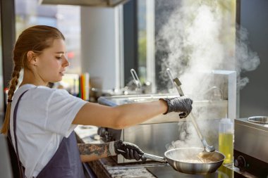 Yetenekli bir şef, modern ve şık bir mutfak alanında içi yemek dolu bir tencereyi ustalıkla karıştırıyor.