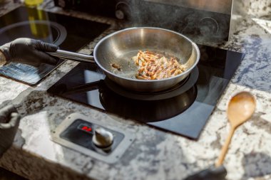 Bir şef paslanmaz çelik bir tavada domuz pastırması pişirir. Parlak bir tezgahın üstünde. Mutfak becerileri sergiliyor..