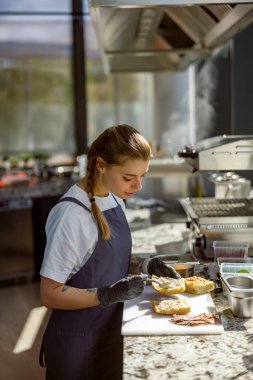 Odaklanmış ve kendini işine adamış genç bir şef modaya uygun, çağdaş bir mutfak ortamında ustaca gurme sandviçler yapar.