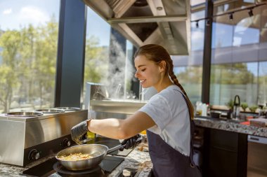 Genç bir şef, güzel bir güneş ışığıyla sıcacık bir mutfakta zevkle lezzetli bir yemek hazırlar.