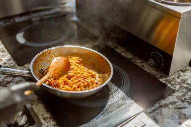 Bu, şık bir mutfak sobasında tavada usulca karıştırılan, dumanı üstünde makarna sergilenen yakın plan bir fotoğraf.