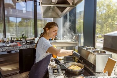 Genç bir kadın, parlak bir mutfakta yemek yapmaktan zevk alır. Modern aşçılık yeteneklerini göstererek.