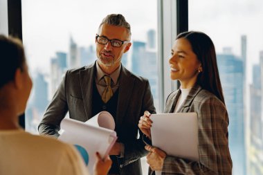İşbirlikçi ve yetenekli profesyoneller şık bir ofis içinde etkileyici bir şehir görüşü sergileyen yenilikçi fikirler hakkında sohbet ediyorlar.