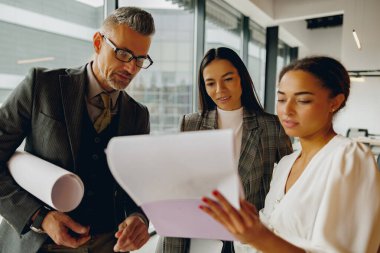 Çeşitli yetenekli profesyonellerden oluşan bir grup modern ofis içinde karmaşık proje detayları üzerinde yakın işbirliği içinde çalışmaktadır.