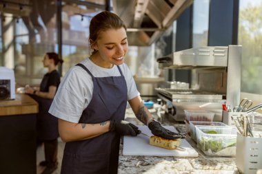 Gülümseyen ve mutlu bir şef şık, güneşli bir mutfak çalışma alanında ustalıkla lezzetli bir sandviç hazırlar.